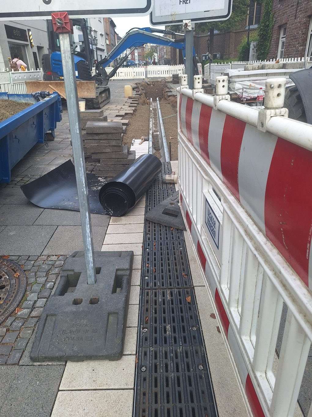 Baustelle in der Süchtelner Fußgängerzone: Die Trasse der bisherigen Regenablaufrinne ist freigelegt, im Hintergrund stehen ein Bagger, ein Container und eine Absperrung.